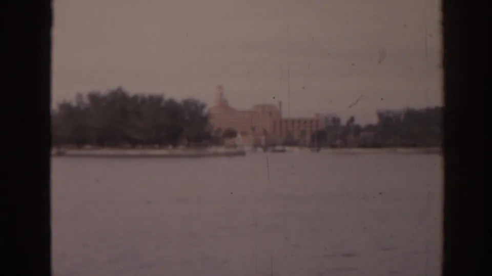 Soft 8mm frame of a Florida waterfront, with trees along the shore and a pale towered building in the distance.