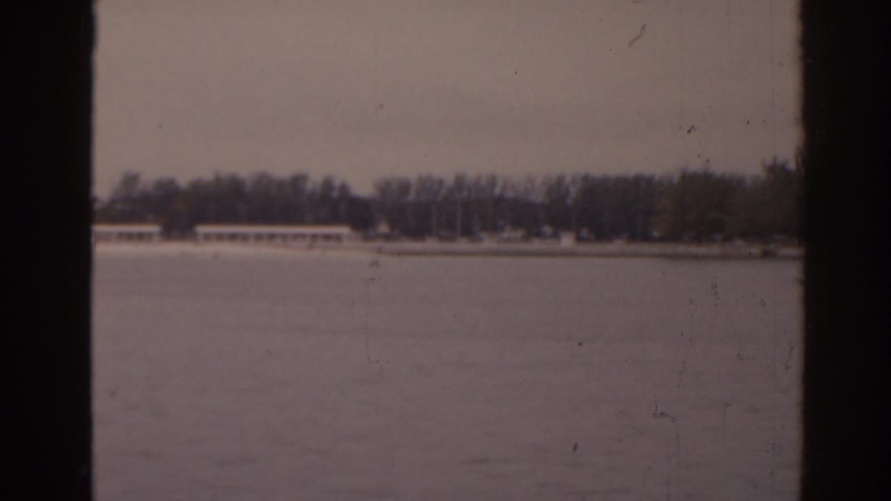 Distant shoreline across a pale water surface, framed by dark film borders.