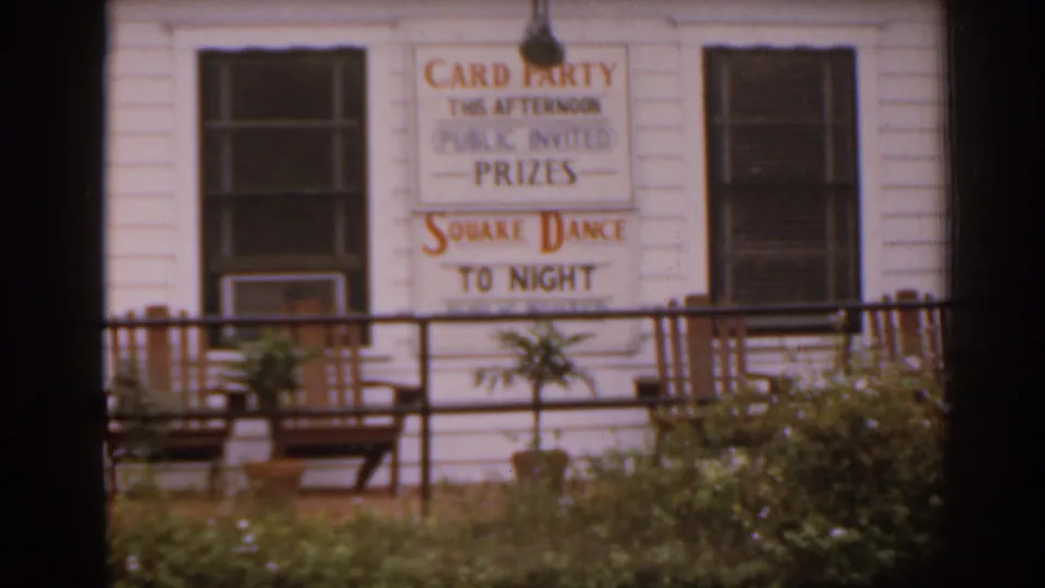 1963 Florida frame showing a white clapboard community building with a sign for a card party and square dance.