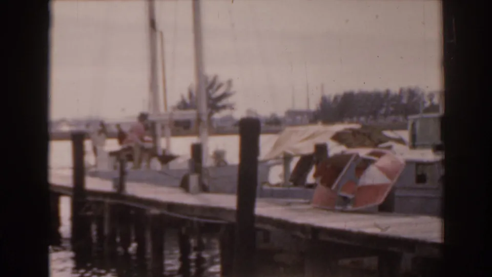 A 1963 Florida marina view shows several small dockside figures near moored boats, wooden pilings, and calm water.
