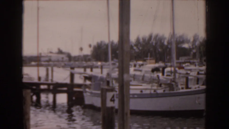 A Florida marina frame shows several docked boats, tall wooden pilings, calm water, and a tree-lined shoreline in soft 8mm color.