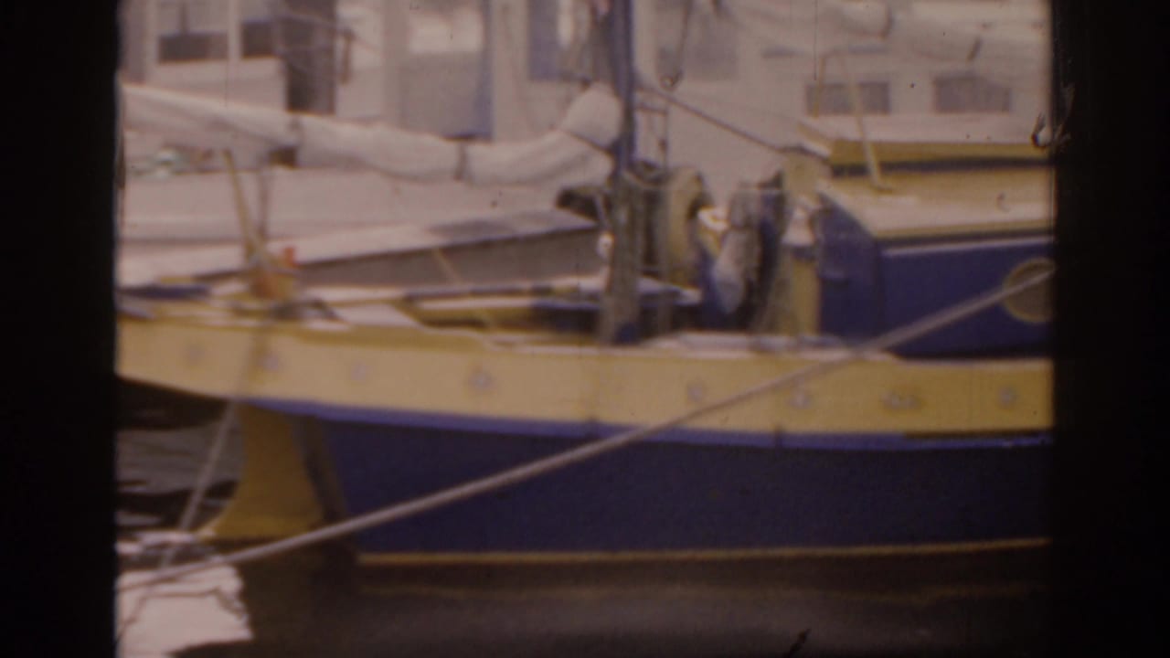 1963 Florida 8mm frame showing a blue and yellow boat docked by wooden pier posts, with cabin details and mooring lines visible.