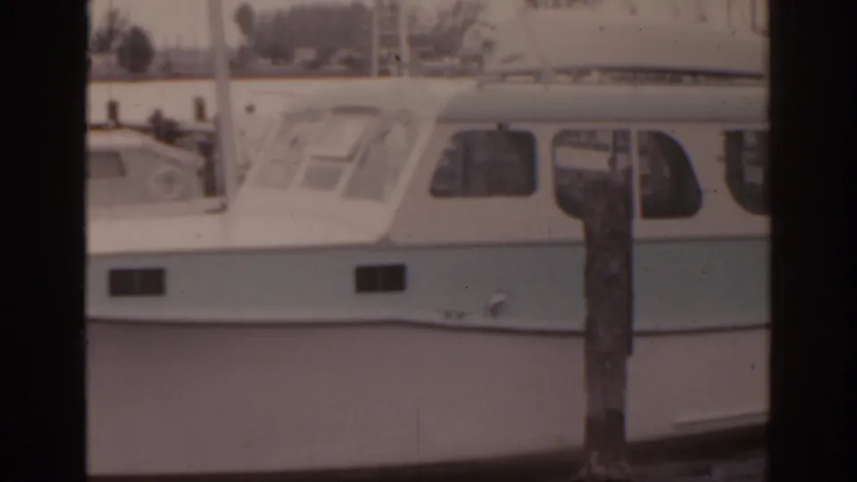 1963 Florida home-movie frame focused on the side of a moored white cabin boat and a weathered wooden piling.