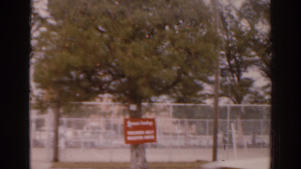 1963 Florida street frame with a red Tampa Adult Education Center sign, trees, fencing, and pale buildings in the background.