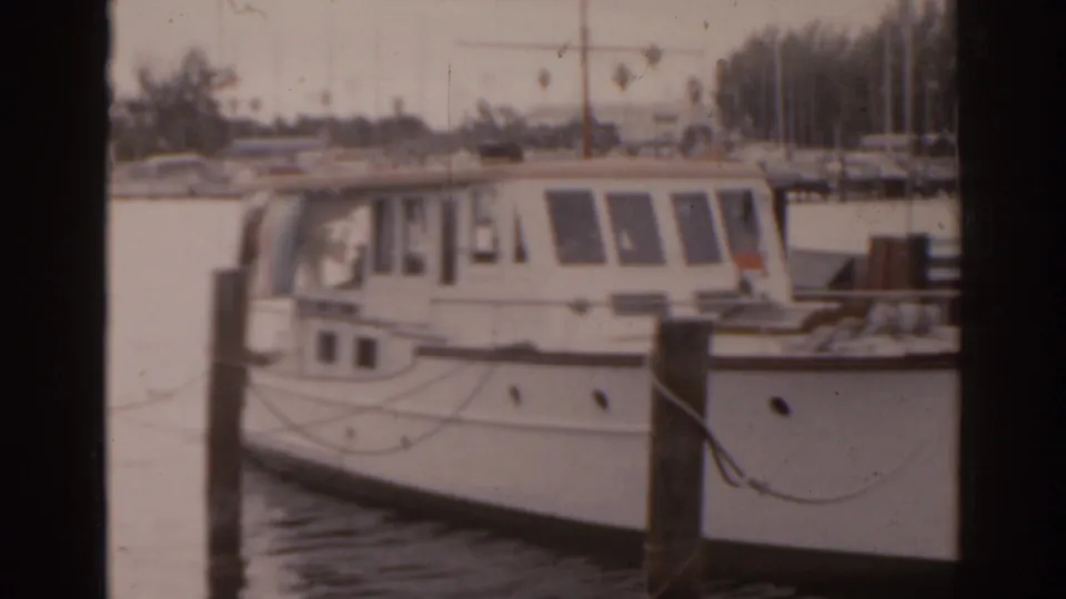1963 Florida marina view with a white cabin motorboat tied beside wooden pilings on calm water.
