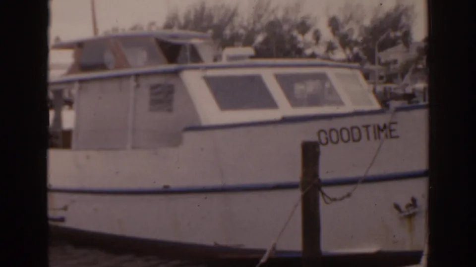 Close 1963 Florida marina frame of a white motorboat, with GOODTIME painted near the stern and a piling in front.
