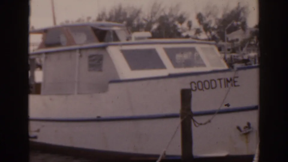1963 Florida home-movie frame showing the white motorboat GOODTIME moored at a marina beside a foreground piling.