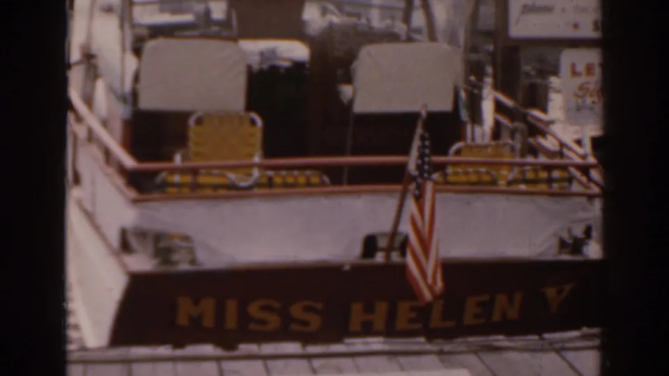 1963 Florida 8mm frame showing the Miss Helen V riverboat stern at dock with an American flag and yellow deck seating.
