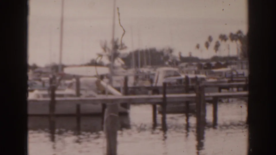 1963 Florida 8mm frame showing small boats docked at wooden piers along calm water, with palms and faint people in the distance.