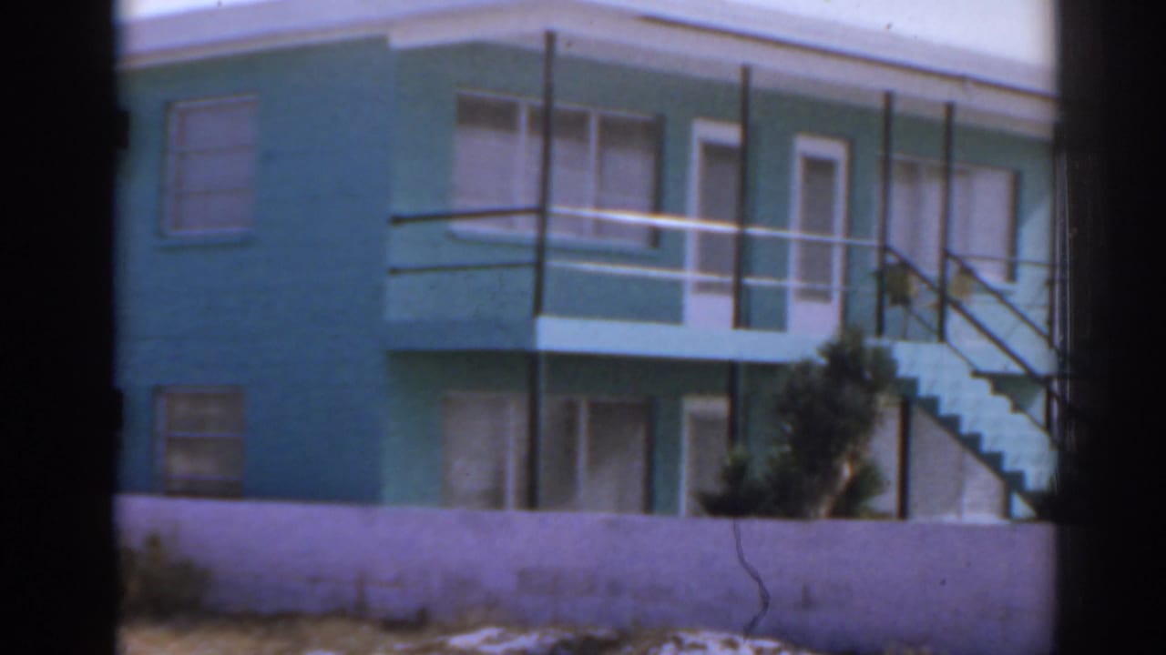 Turquoise beachfront building with white trim, balcony, and exterior stairs.