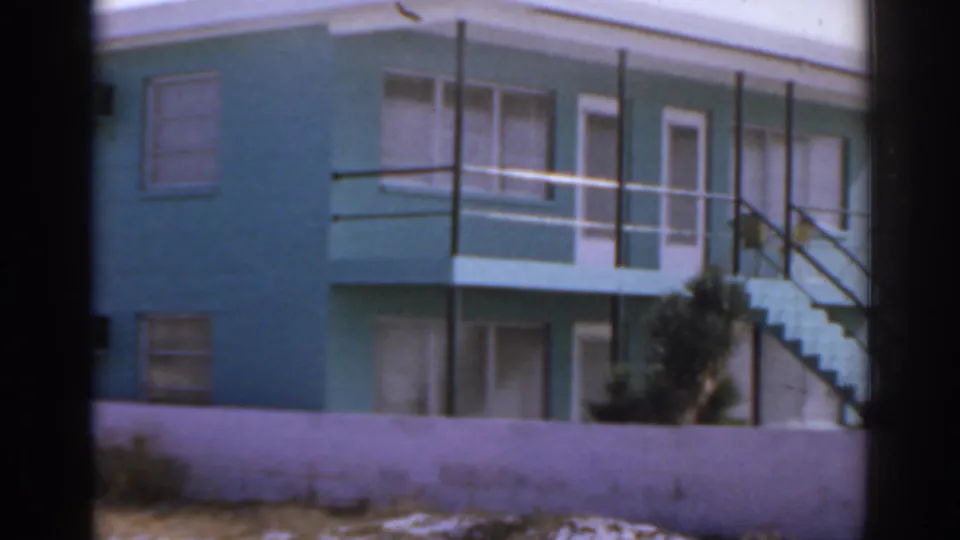 1963 Florida home-movie view of the turquoise beachfront structure, white balcony railings, exterior stairway, and foreground wall.
