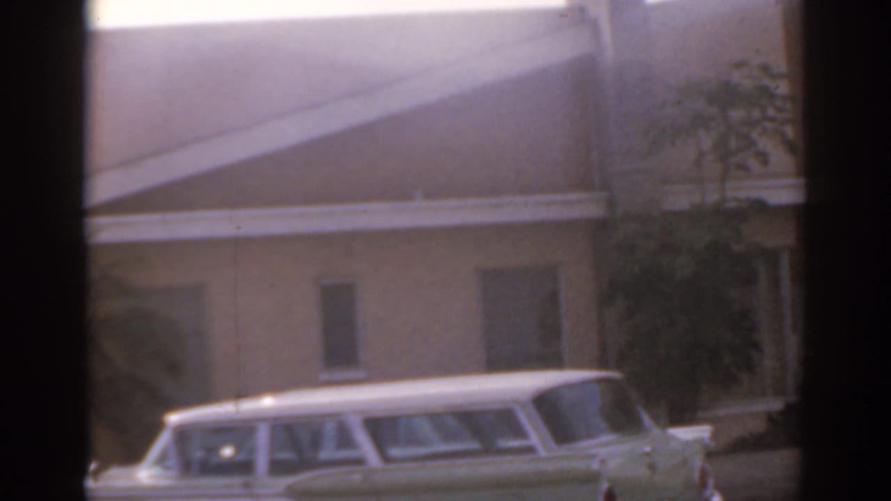 White station wagon parked beside a low building near a broad street.