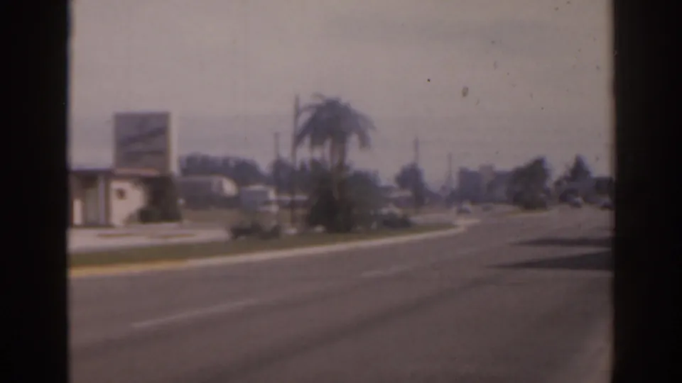 1963 Florida home-movie frame showing a quiet broad avenue, palm trees, low buildings, and faded film color.