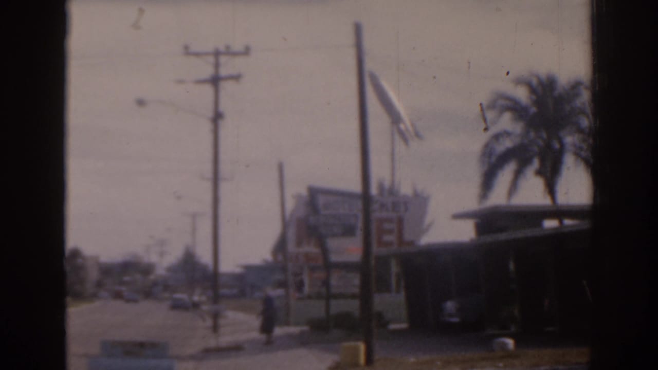 Roadside view with utility poles, motel signage, palm trees, cars, and a pedestrian near the sidewalk.