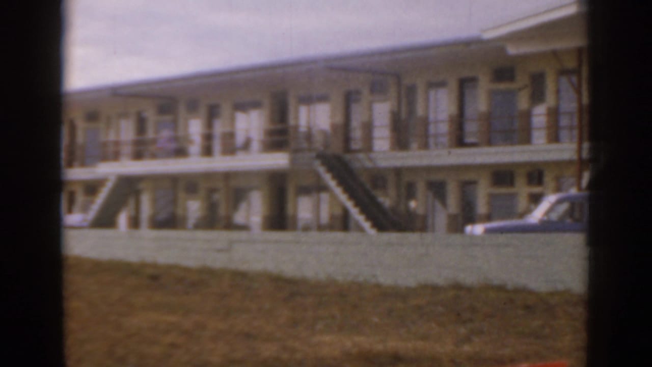 Yellow two-story beachfront building behind a low wall with exterior stairs and balconies.