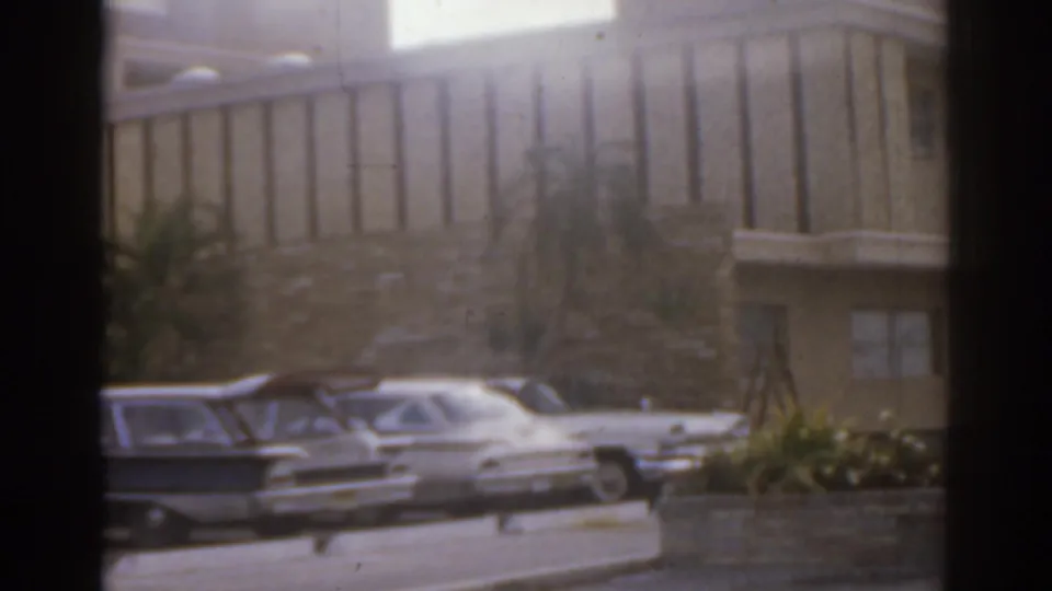 1963 Florida 8mm view of parked cars beside a mid-century building with palms and low landscaping.