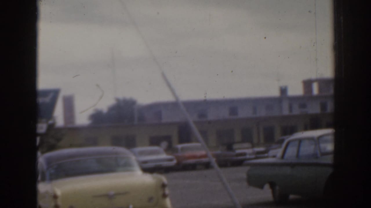 Yellow sedan and other parked cars near a roadside building, with dark frame bars crossing the view.
