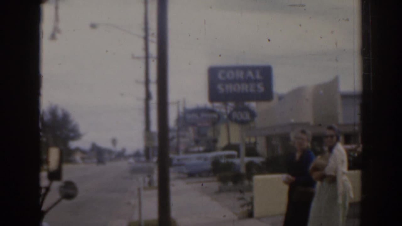 Two women stand near a Coral Shores motel sign beside a Florida street.