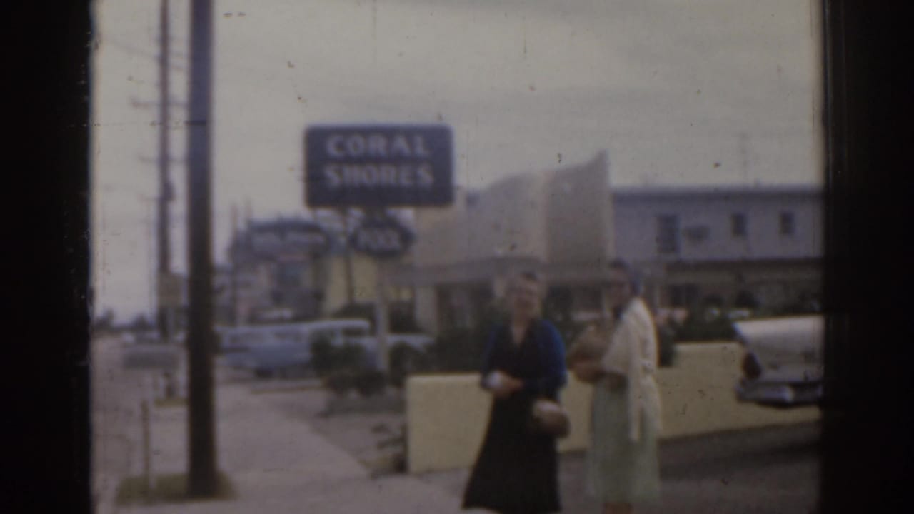 Two women stand by a low wall near the Coral Shores sign and roadside motel.
