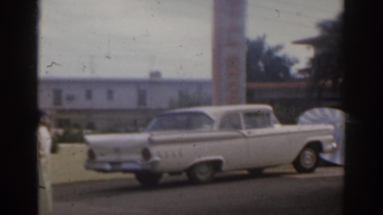 White classic car parked on a street seen through dark window framing.