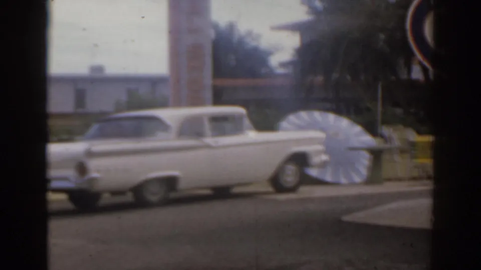 White classic car parked on a Florida street in 1963, with a fan-shaped display and motel buildings behind it.