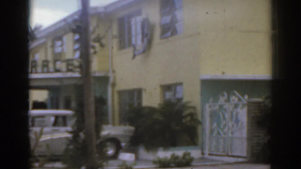 Yellow Florida motel facade with ornate gate, balcony details, plants, and a car partly visible in a 1963 home-movie frame.