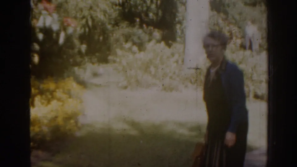 Brief 1963 Florida home-movie glimpse of an adult in dark clothing passing through a sunlit garden setting.