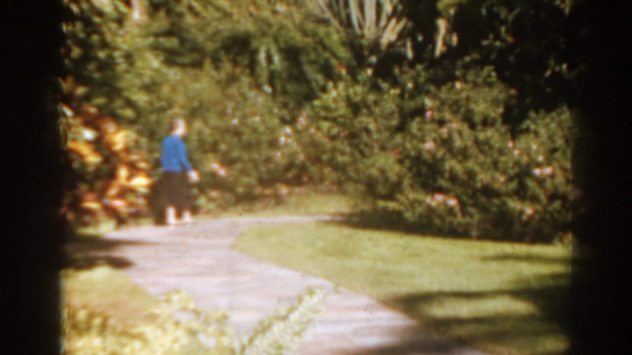 Woman in a blue sweater walking along a curved garden path.