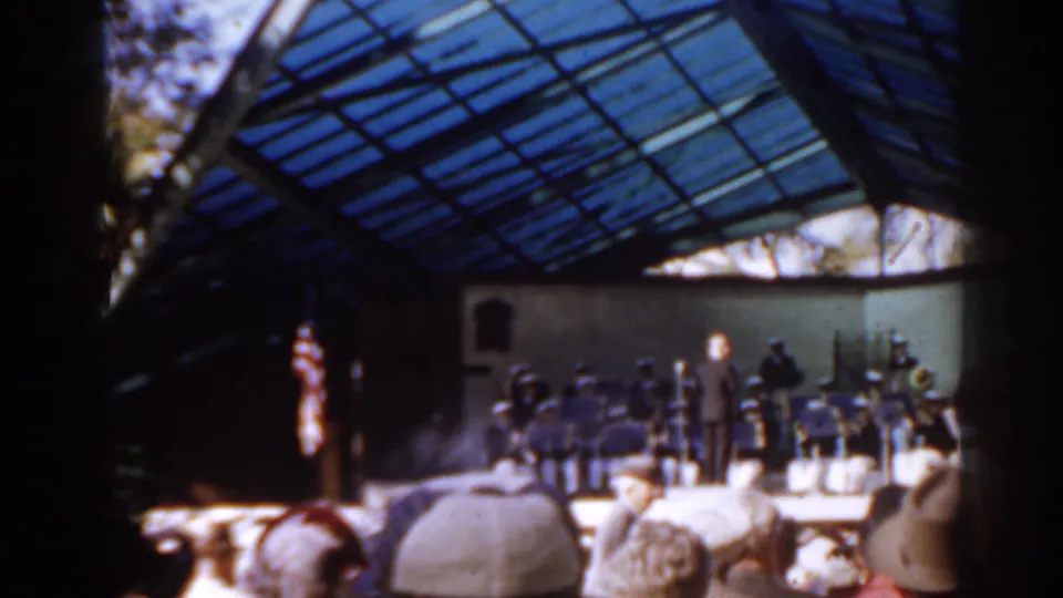 A band performs beneath a glass-roofed pavilion while spectators watch from rows of seats in 1963 Florida home-movie footage.
