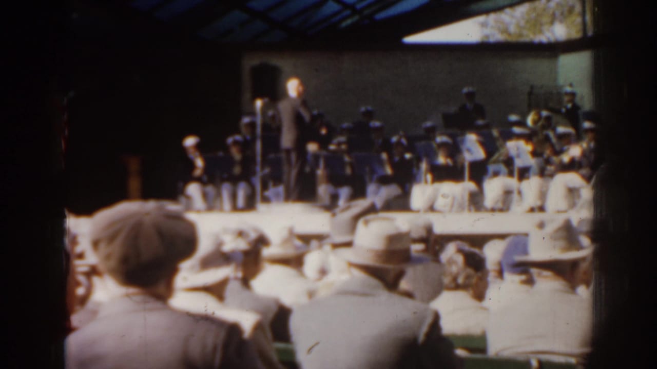 Audience seated before an outdoor orchestra on a raised stage.