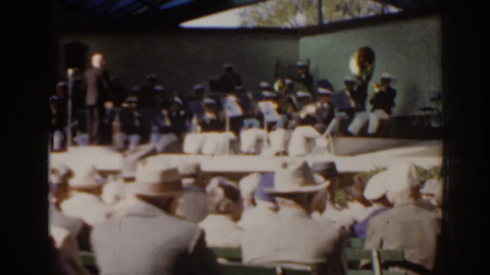 Late-frame view of the 1963 Florida outdoor orchestra scene, with spectators in the foreground and brass players at right.