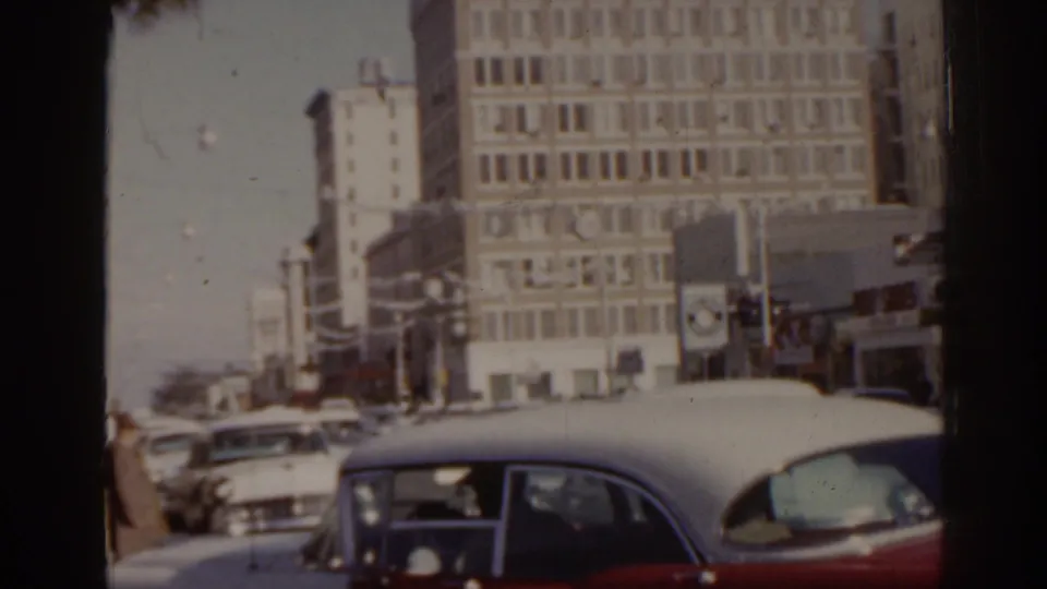 1963 Florida street view with classic automobiles, pedestrians near an intersection, traffic lights, and mid-century commercial buildings.
