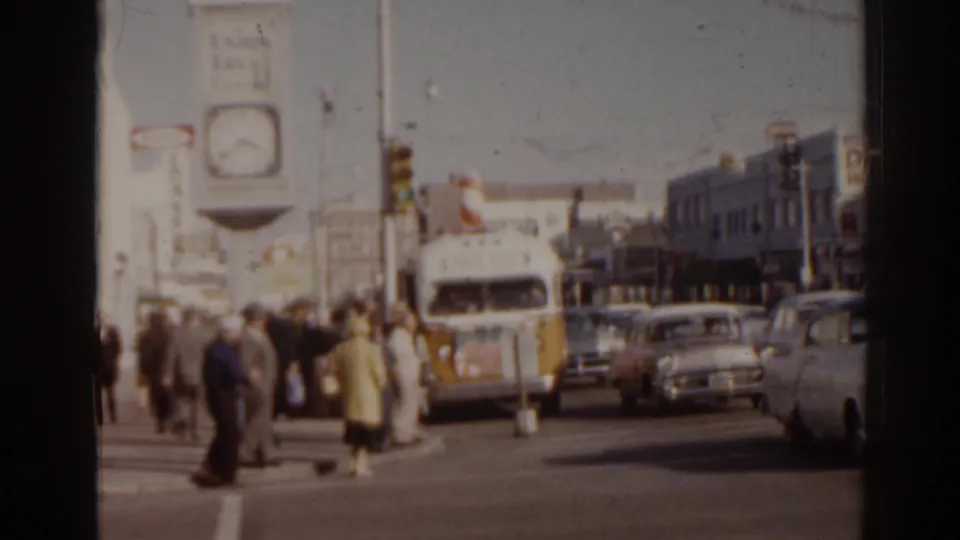 1963 Florida street scene showing pedestrians at a crosswalk, a decorated bus, classic automobiles, and commercial buildings in the background.