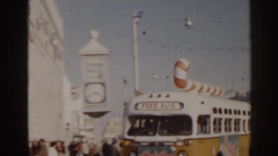 1963 Florida close street view of a white-and-yellow bus marked as a free bus, with candy cane decoration and a large street clock nearby.