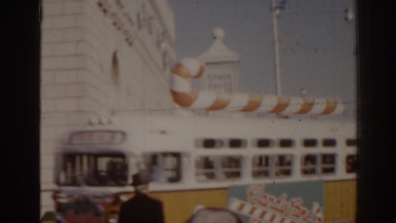 Decorated white-and-yellow bus passing a street corner with a pedestrian and building facade.