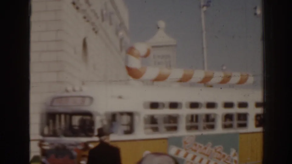 1963 Florida home-movie frame showing a candy-cane-decorated bus, a pedestrian, and a light-colored building along a city street.