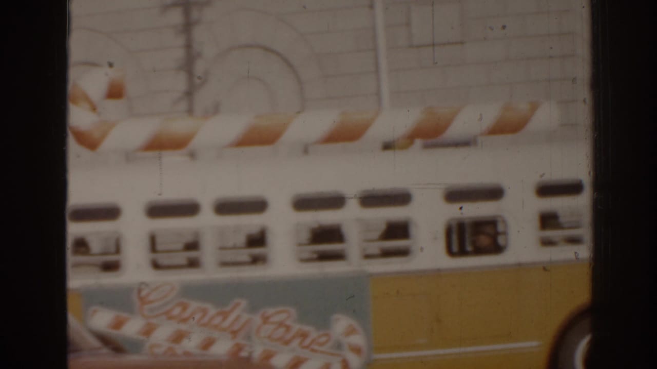Side of a white-and-yellow decorated bus moving past a pale building.