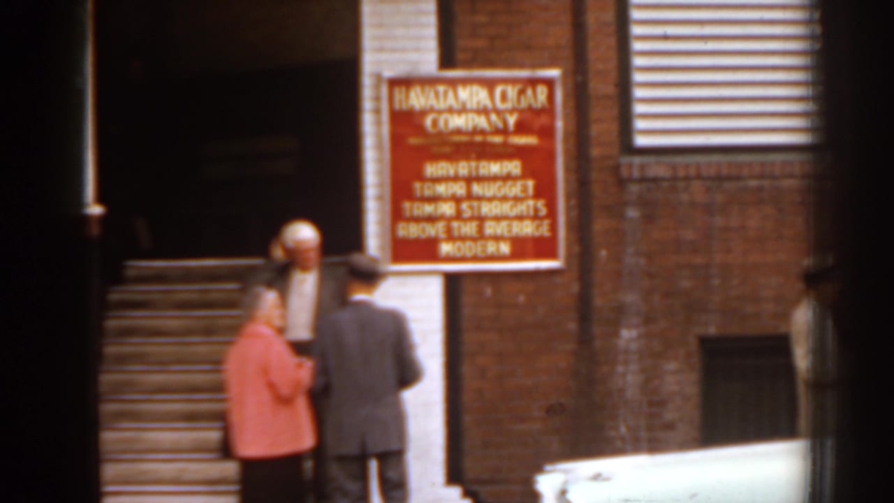 Brick storefront with Havatampa Cigar Company sign and several adults near the steps.