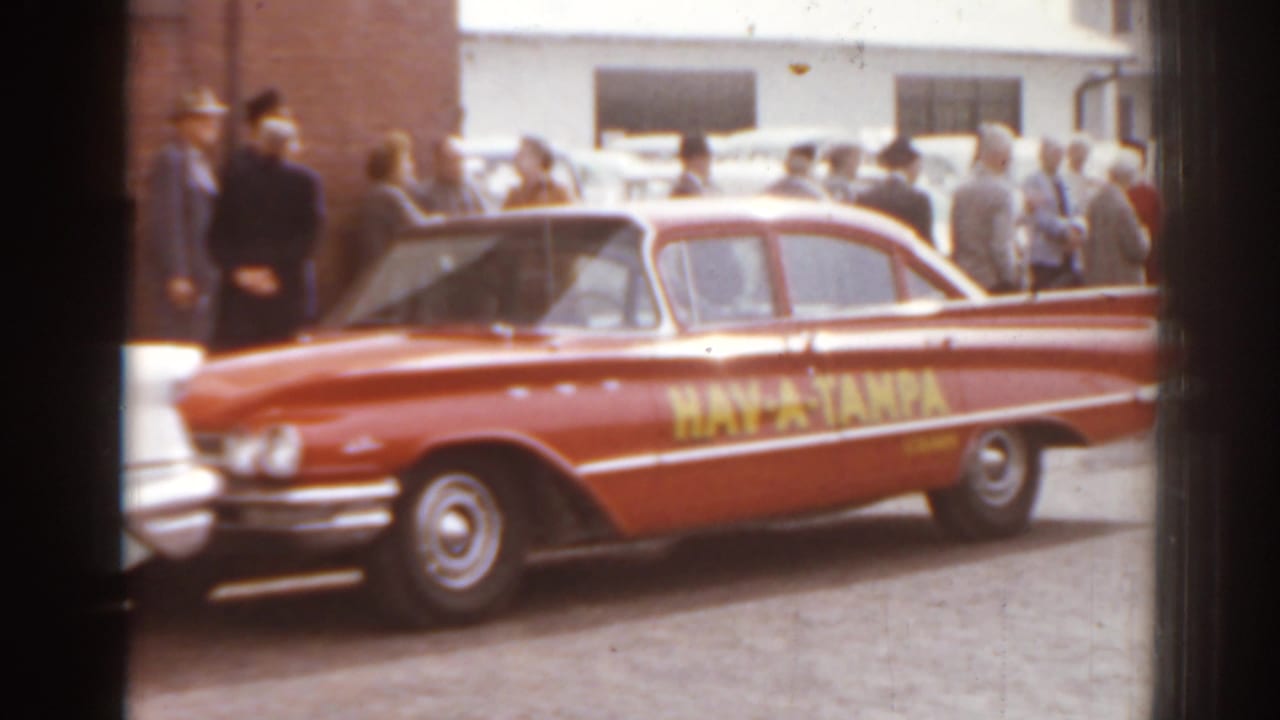 Red Hav-A-Tampa car parked beside a crowd on a street.