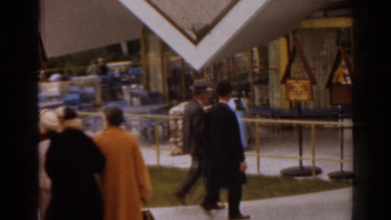 Adults in mid-century clothing walk past angular modernist structures and railings.