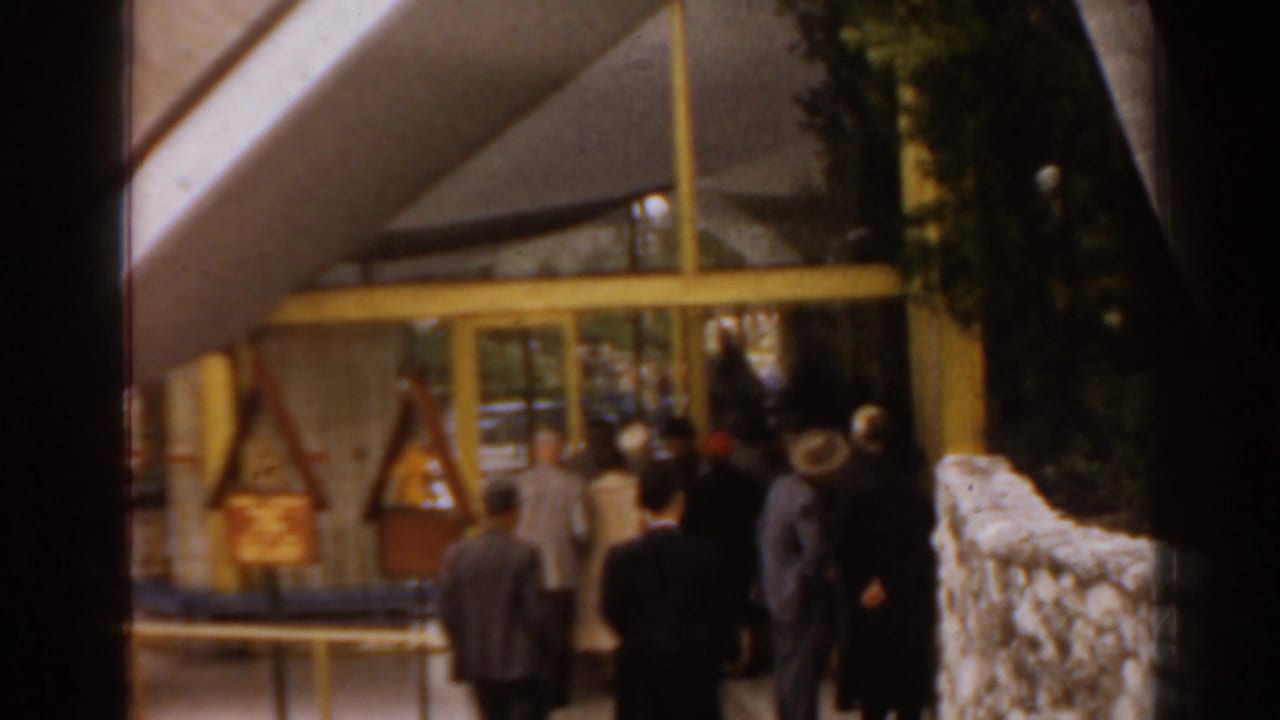 A group of adults approaches a glass-fronted structure beside a stone wall.
