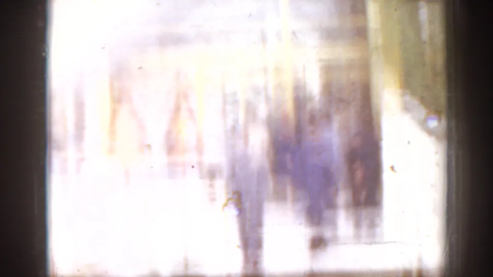 Overexposed 8mm frame from the 1963 Florida clip, with faint adult figures and architectural forms partly washed out by light.
