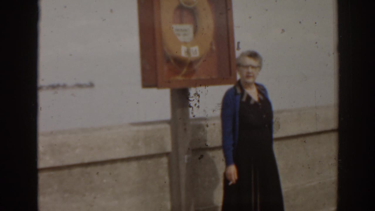 Woman by a life preserver cabinet on a pier, framed through film gate edges.