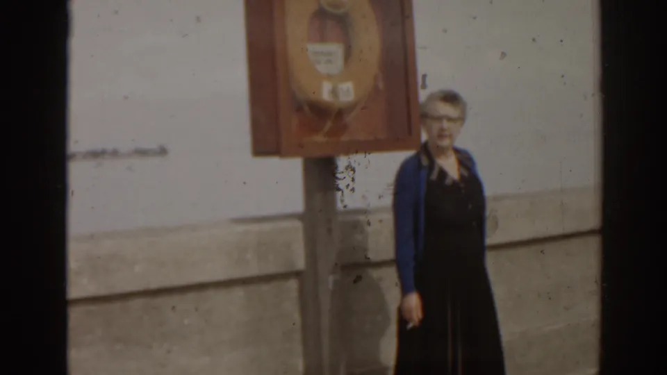 A woman stands on a Florida pier near a wall-mounted life preserver cabinet, with soft 8mm focus and visible film wear.