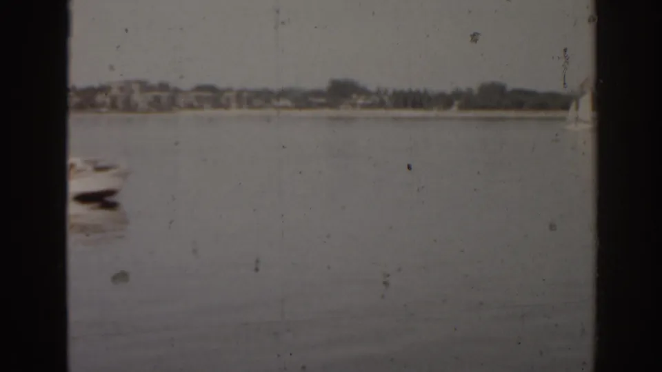 A calm Florida waterfront view shows a small boat at left and a low distant shoreline beyond the water.