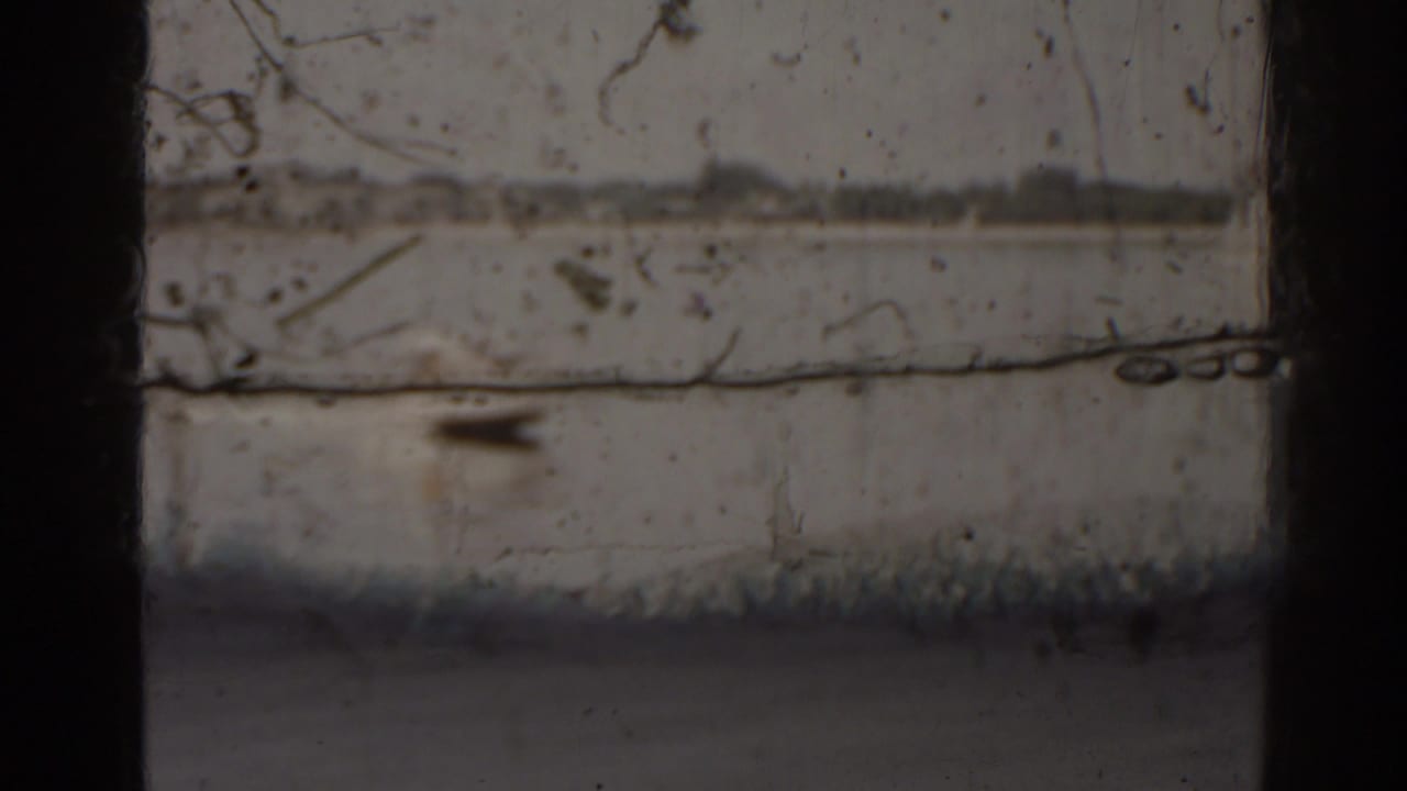 Distant motorboat on a lake viewed through dark vertical window framing.