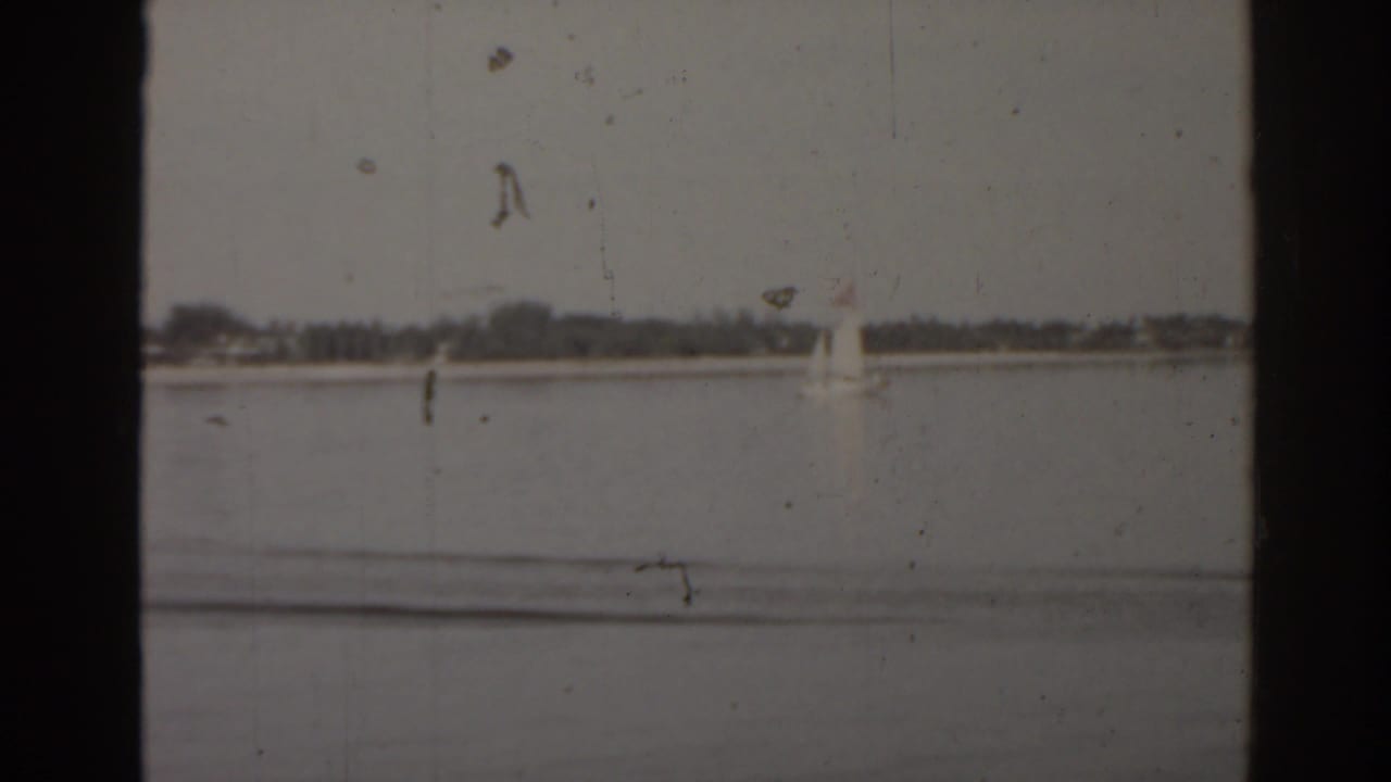 Small sailboat on open lake water with a low distant shoreline.
