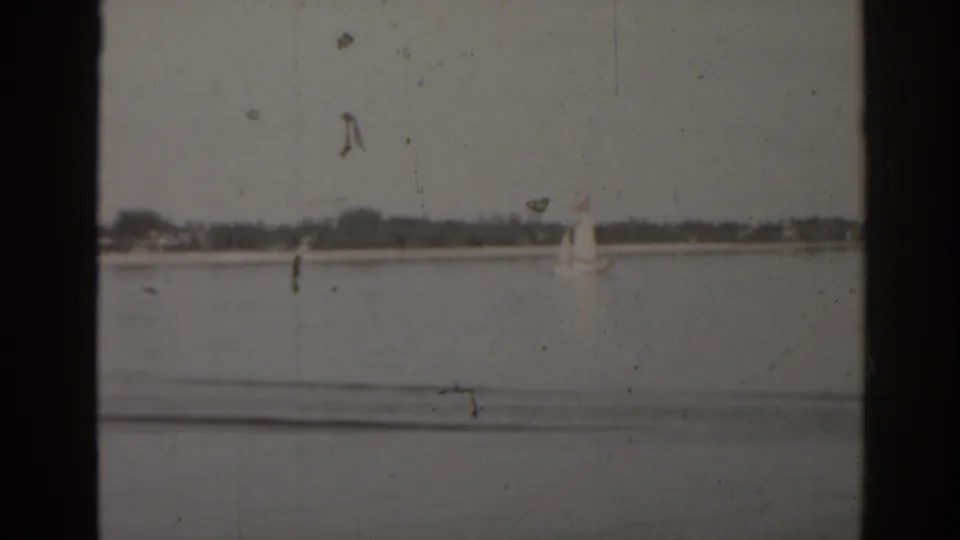 1963 Florida lake view with a small white sailboat near the horizon and a low shoreline beyond the water.