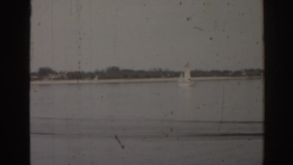 1963 Florida 8mm view of a small sailboat on calm lake water, with dark foreground framing and visible film marks.