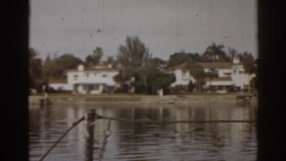 1963 Florida lake view with soft 8mm texture, white waterfront houses, trees, reflections, and a foreground railing.